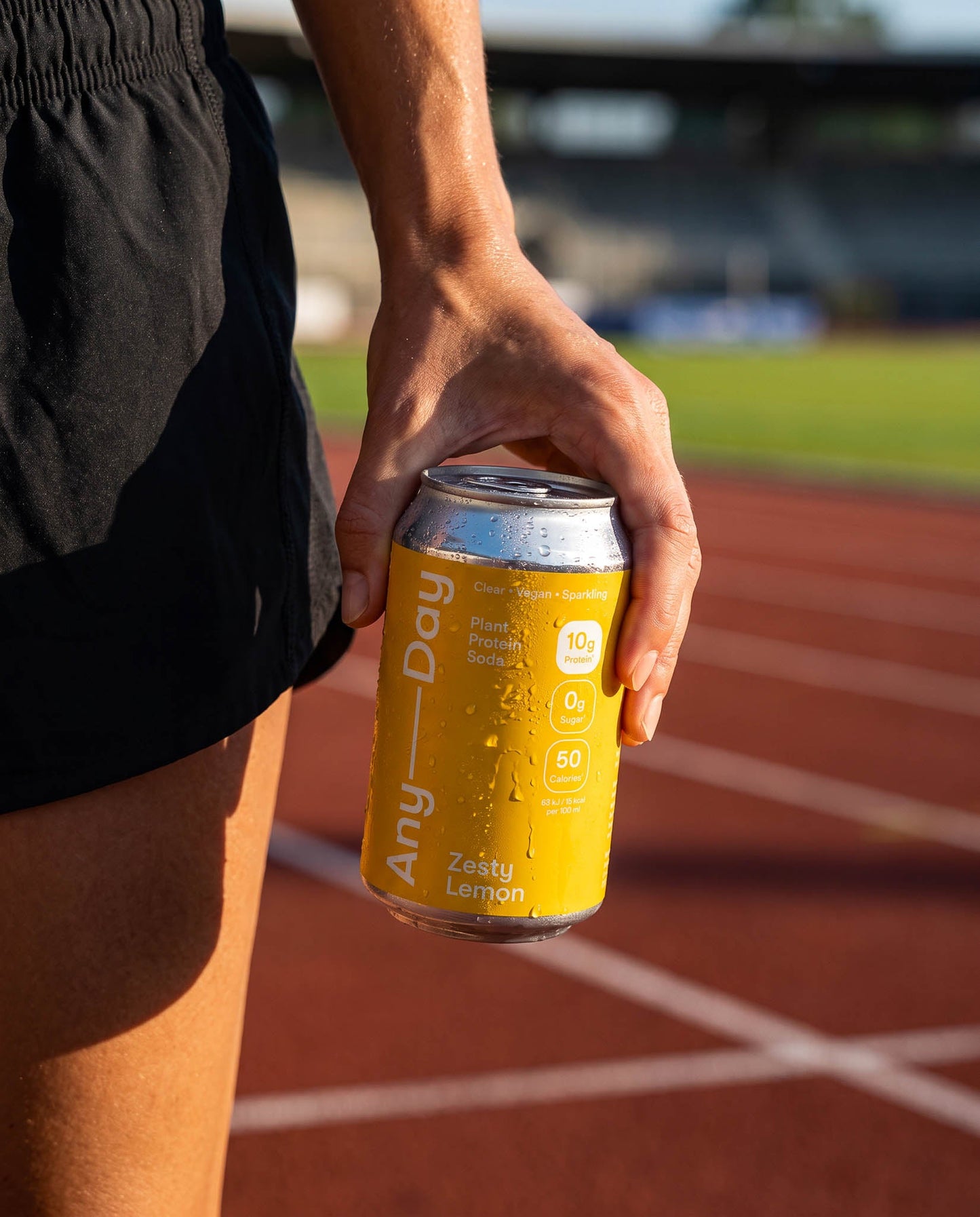 Sportlerin hält eine Dose Anyday Plant Protein Soda Zesty Lemon auf einer Laufbahn nach dem Training.